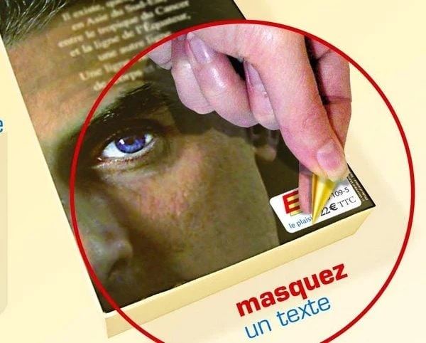 Application à la main d'une étiquette rectificative opaque sur le prix imprimé d'un livre, pour masquer le texte d'origine